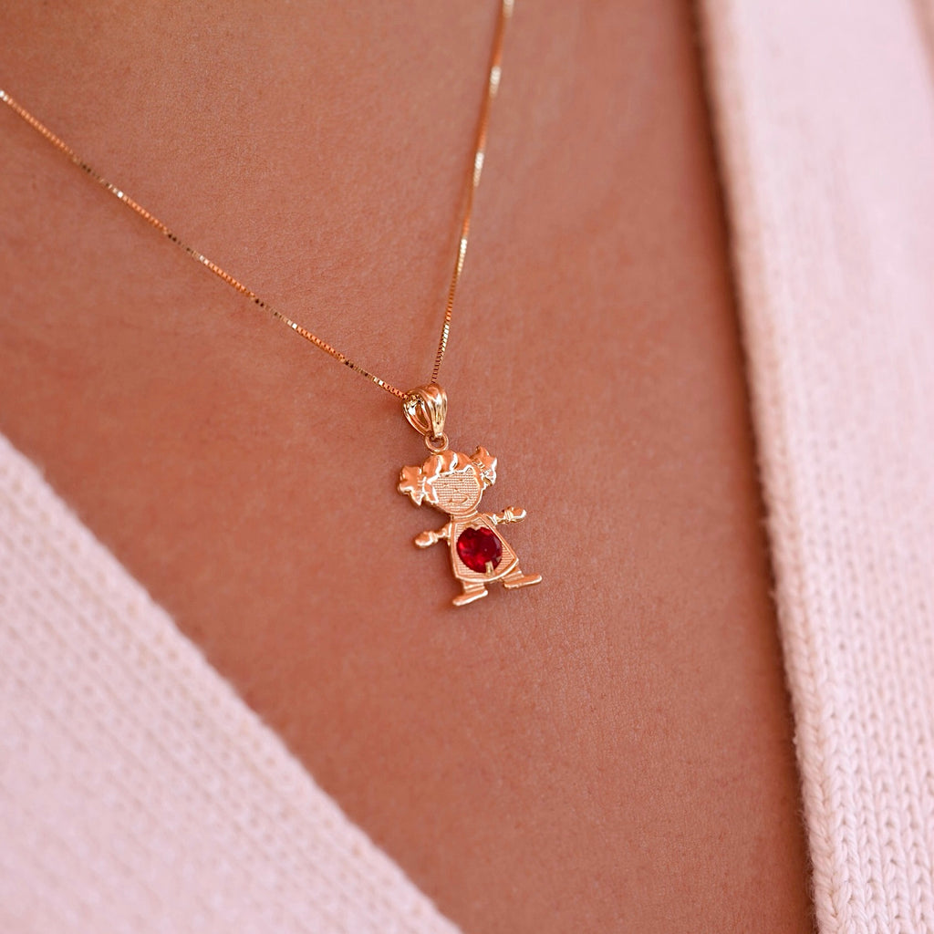 Woman wearing 14K gold girl charm pendant with red cubic zirconia birthstone on a chain necklace.