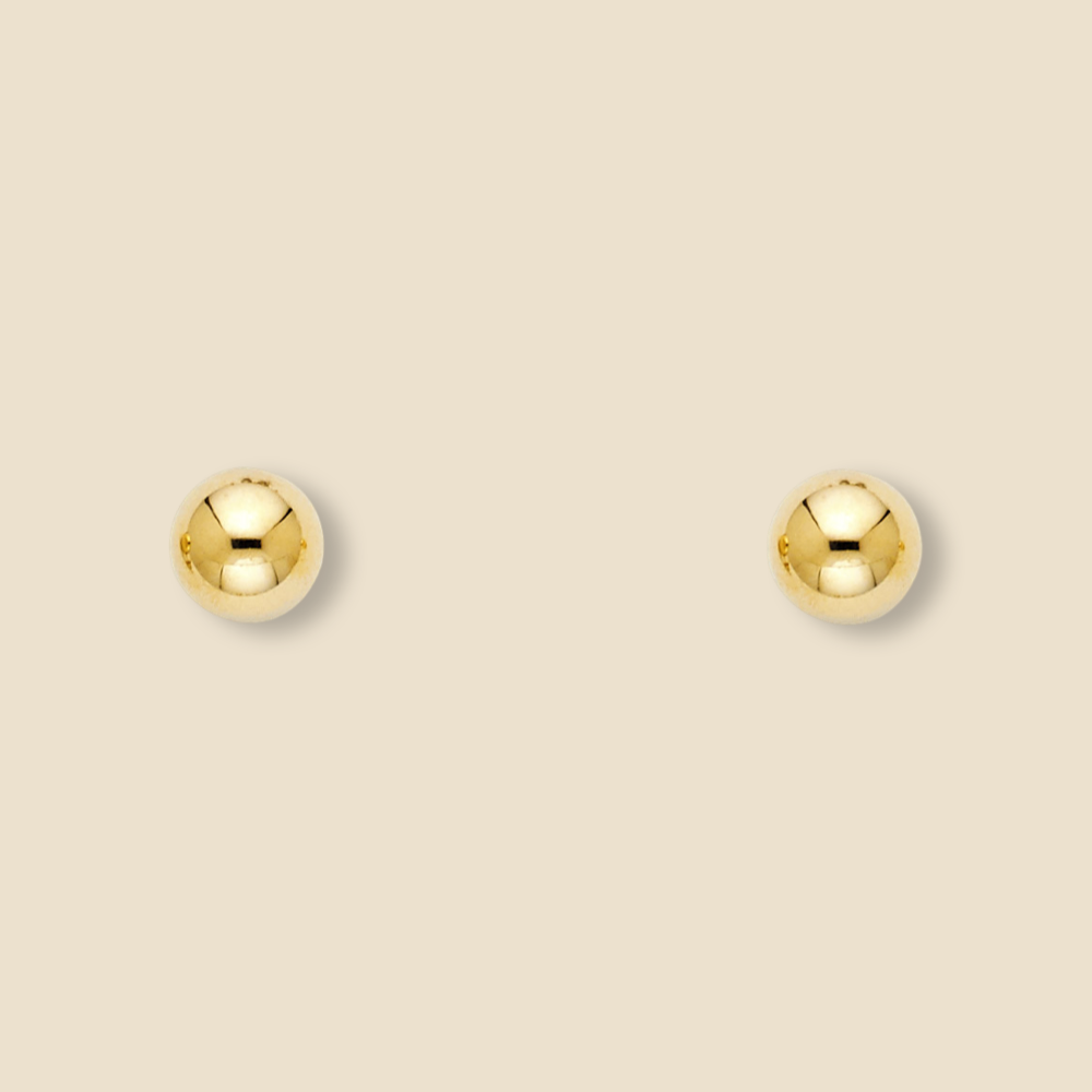Studio image of polished 14K yellow gold ball earrings laid on a plain background, revealing size and brilliance.