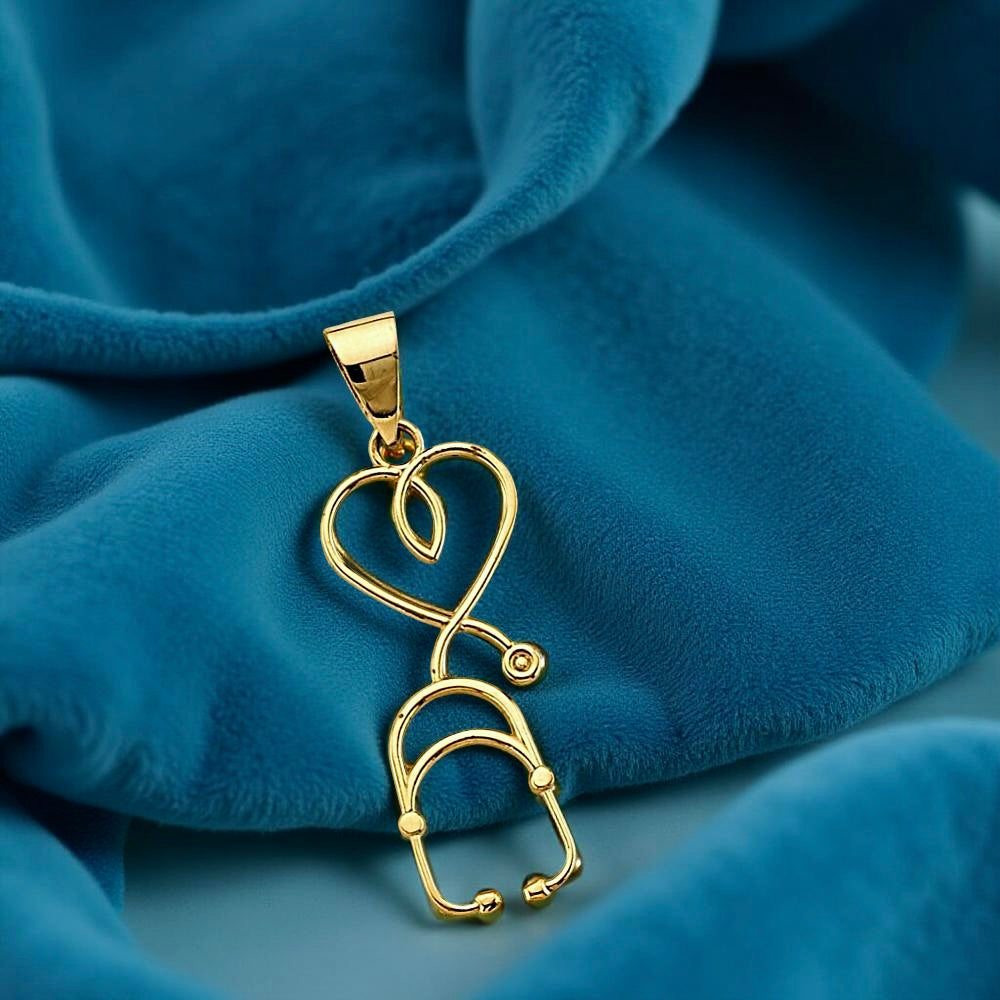 Close-up of a dainty 14K gold stethoscope pendant resting gently on a blue fabric surface, with soft lighting enhancing the rich yellow tones and showcasing its sleek curves, ideal for medical professionals or healthcare gifts.