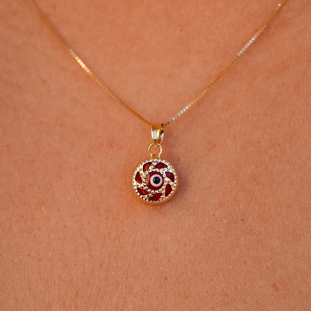 A model is wearing the 14K gold Evil Eye pendant with a red eye on a fine chain, allowing the charm to rest beautifully against the skin. The striking red eye adds a subtle yet meaningful touch, perfect for everyday wear.