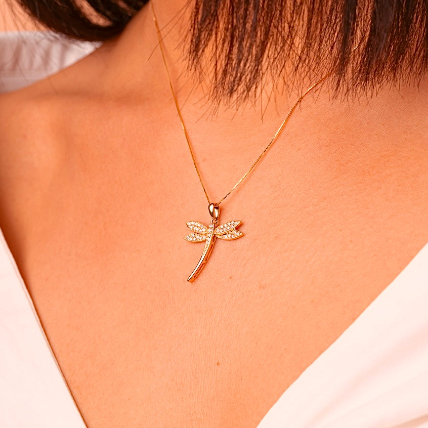 A close-up of a model wearing the 14K gold dragonfly pendant on a fine gold chain. The pendant sits gracefully on the collarbone, catching the light with its cubic zirconia details for a sophisticated, nature-inspired look.