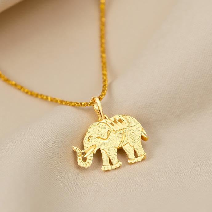 14K gold elephant pendant resting on a cream textured cloth, showing its dainty shape and smooth polished finish.