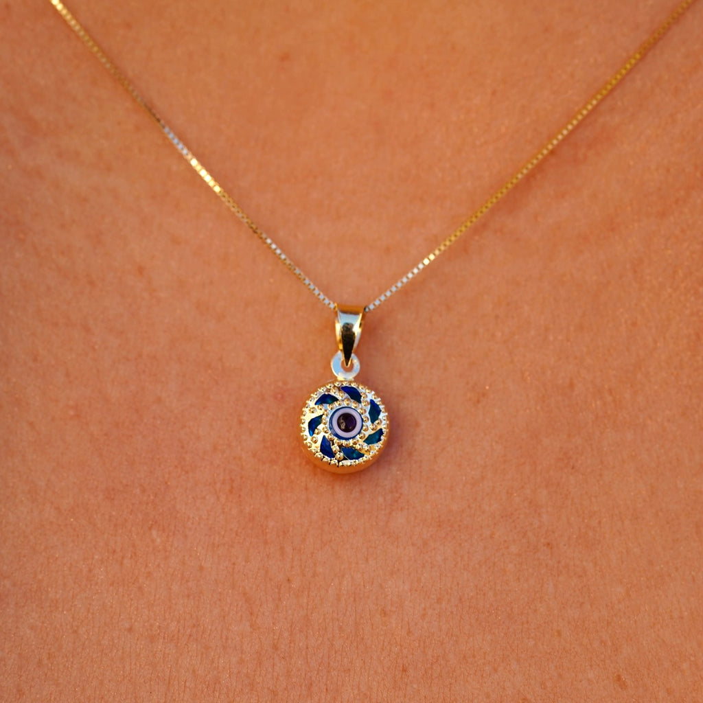 A model is wearing the 14K gold Evil Eye pendant with a blue eye on a fine chain, allowing the charm to rest beautifully against the skin. The striking blue eye adds a subtle yet meaningful touch, perfect for everyday wear.