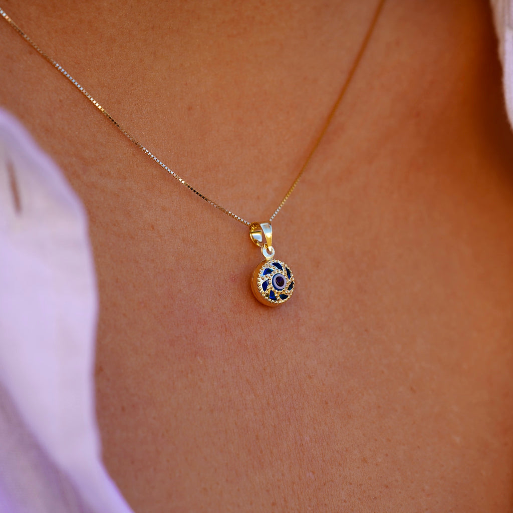A model is wearing the 14K gold Evil Eye pendant with a blue eye on a fine chain, allowing the charm to rest beautifully against the skin. The striking blue eye adds a subtle yet meaningful touch, perfect for everyday wear.