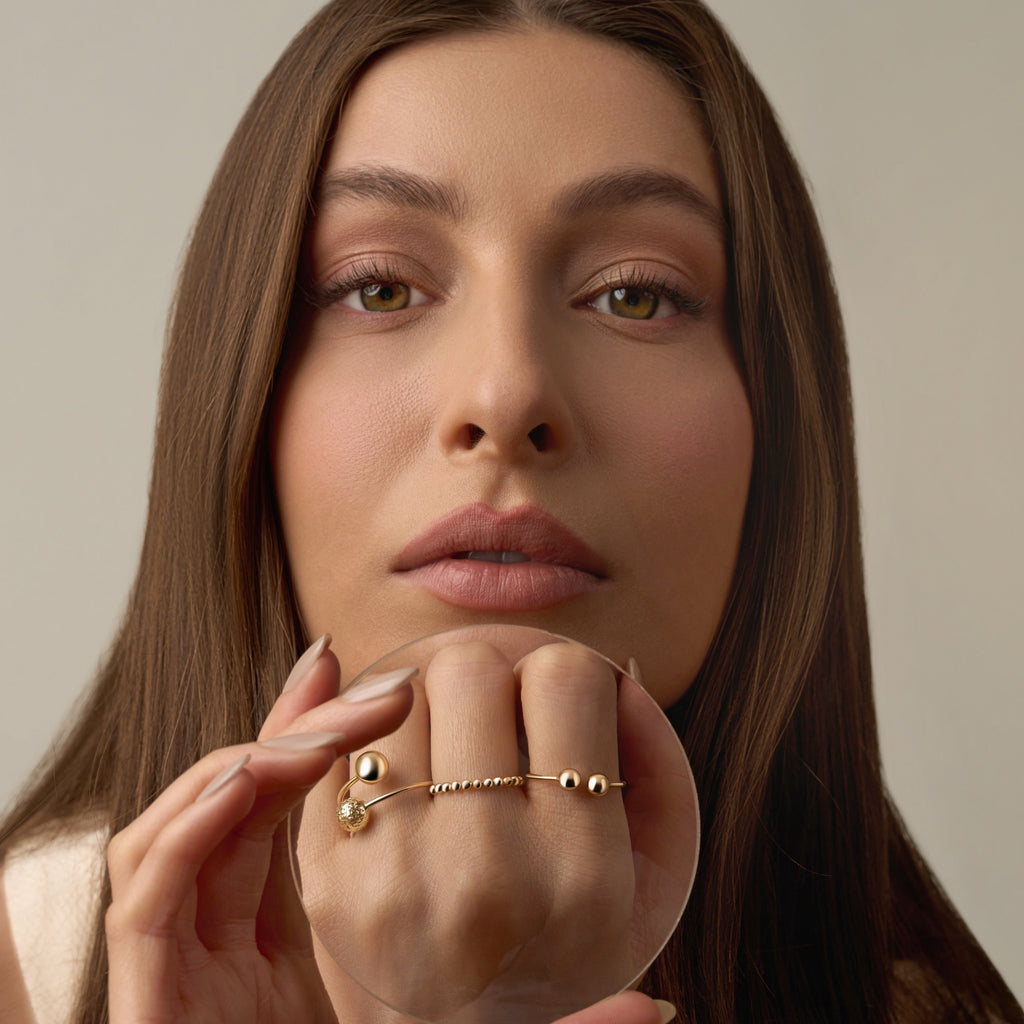 A model’s hand adorned with several rings, featuring the 14K yellow gold polish ball ring with polished beaded detailing. The minimalist, stackable design adds subtle shine and refined elegance, complementing the other rings for a modern, layered look.
