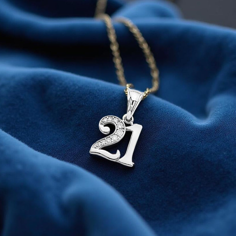 14K white gold '21' pendant with sparkling CZ accents displayed on soft blue velvet fabric, highlighting its elegant shine and detailed craftsmanship.