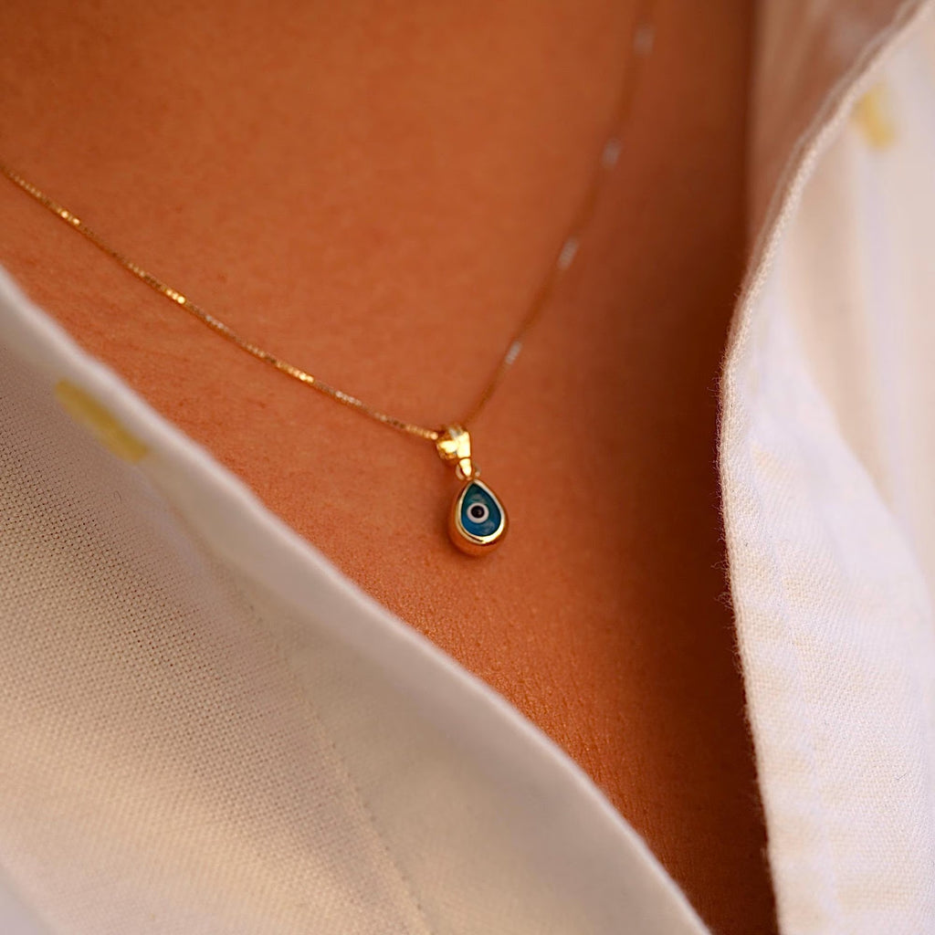 A model wears the 14K Gold Tiny Tear Evil Eye Charm with the vibrant blue eye, adding a touch of protection and elegance to her necklace.