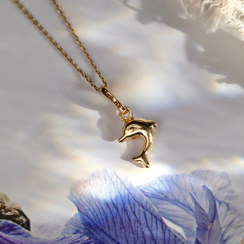 14K Solid Gold Dolphin Pendant with a high-polished finish, showcasing fine craftsmanship and delicate details against a white and blue backdrop.