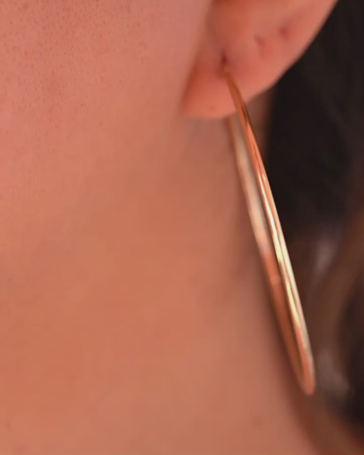 A woman wearing the 14K gold hoop earrings, highlighting their lightweight yet bold design, adding an elegant touch to her stylish outfit.