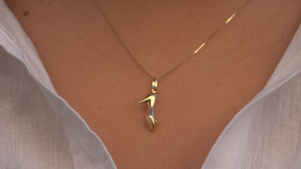 Video of a model wearing the 14K Gold Heel Shoe Charm Pendant, showcasing its delicate high heel design, polished yellow gold finish, and elegant movement on a chain.