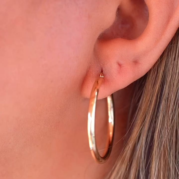 A stylish woman wearing 14K gold hoop earrings in yellow and white gold, adding a touch of sophistication to her everyday look.