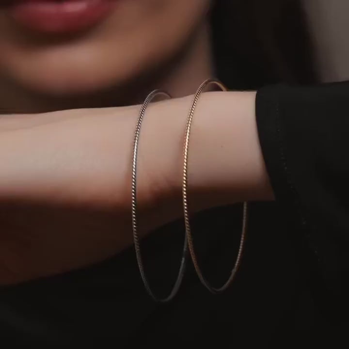A model wearing 14K gold braided bangle on her wrist, showcasing its delicate 1.5mm rope-inspired design. The bangle shines in a polished yellow gold finish, highlighting its elegant, lightweight, and dainty texture. The image demonstrates how the bangle can be worn alone for a minimalist look or stacked with other bracelets for a layered, sophisticated style, perfect for everyday wear or special occasions.