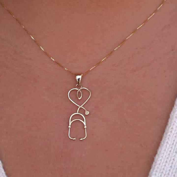 A model wears the 14K yellow gold stethoscope pendant on a delicate gold chain, showcasing its sleek vertical design against a neutral outfit.
