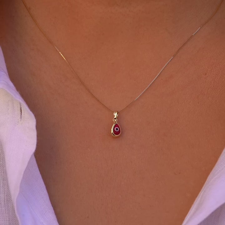 Video of a model wears the 14K Gold Tiny Tear Evil Eye Charm with the vibrant red eye, adding a touch of protection and elegance to her necklace.
