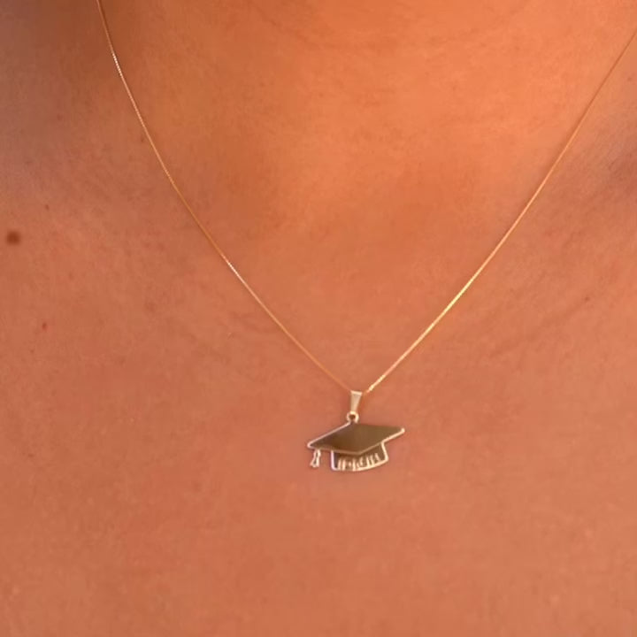 A model elegantly wears the 14K solid gold graduation cap pendant on a delicate chain, showcasing its brilliant shine and meaningful design. The charm rests beautifully against the skin, making it a perfect way to commemorate this special milestone.