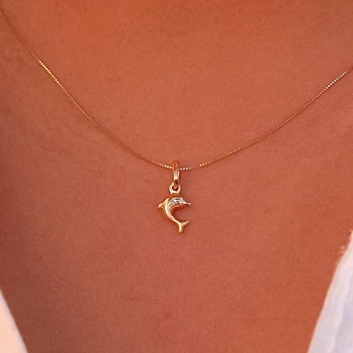 Model wearing the 14K yellow gold dolphin pendant on a fine chain, demonstrating its dainty size and stylish appeal.