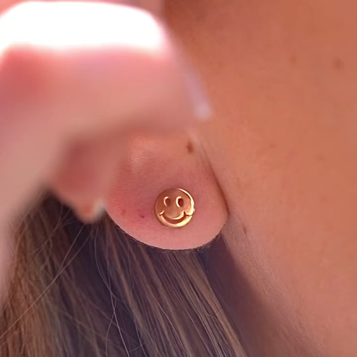 Close-up of a model wearing the 14K Yellow Gold Smiling Emoji Stud Earrings, showcasing their fun and playful design with a secure screw-back closure.
