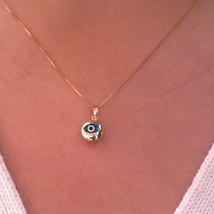 A model wearing a 14K yellow gold evil eye pendant with a blue zirconia center on a fine gold chain, resting elegantly at her collarbone. The polished gold finish reflects light beautifully, highlighting the pendant’s delicate craftsmanship, symbolic protection, and subtle luxury from Tehrani Jewelry.
