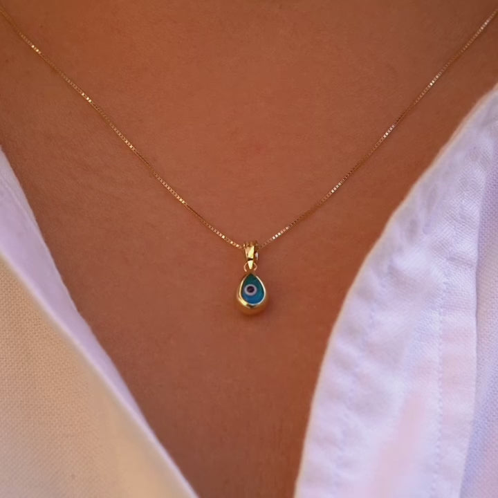 Video of a model wears the 14K Gold Tiny Tear Evil Eye Charm with the vibrant blue eye, adding a touch of protection and elegance to her necklace.