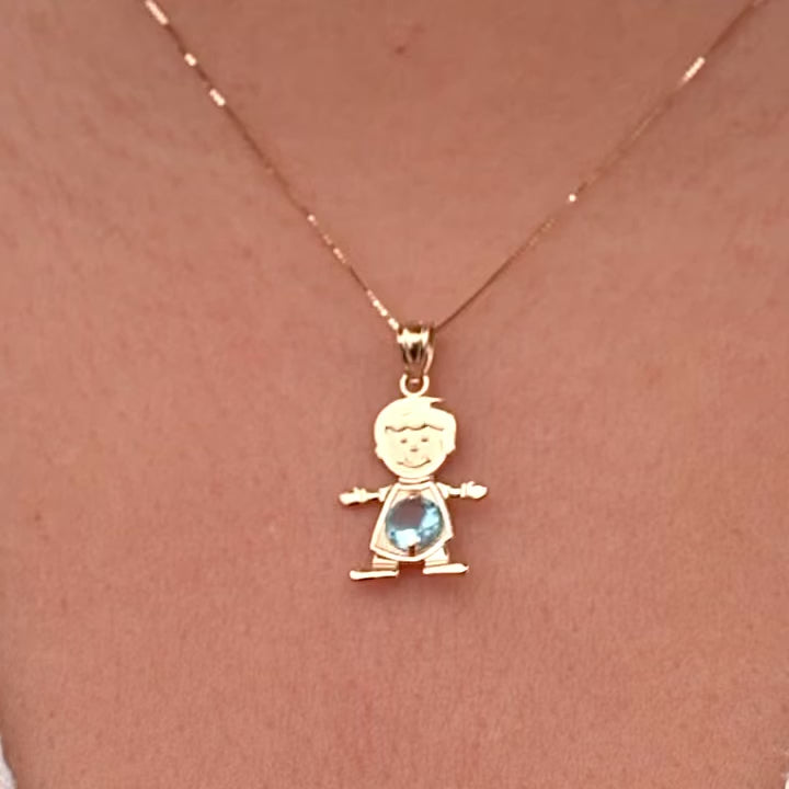 Model wearing a 14K solid gold boy charm necklace featuring a light blue cubic zirconia birthstone for March, layered with other gold chains, creating a stylish, personalized jewelry stack against a light sweater.