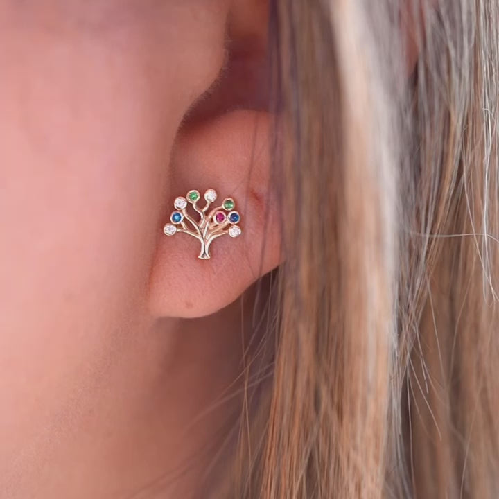 A video of a woman wearing the 14K gold Tree of Life earrings, with the delicate studs resting gracefully on her earlobes. The polished gold and radiant Cubic Zirconia catch the light, adding a subtle yet sophisticated touch to her look.