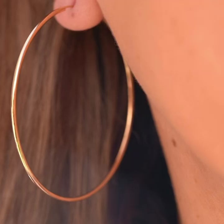 A model wearing 14K Yellow Gold 1.5mm Endless Hoop Earrings (55mm), highlighting their large size and elegant style for everyday wear.