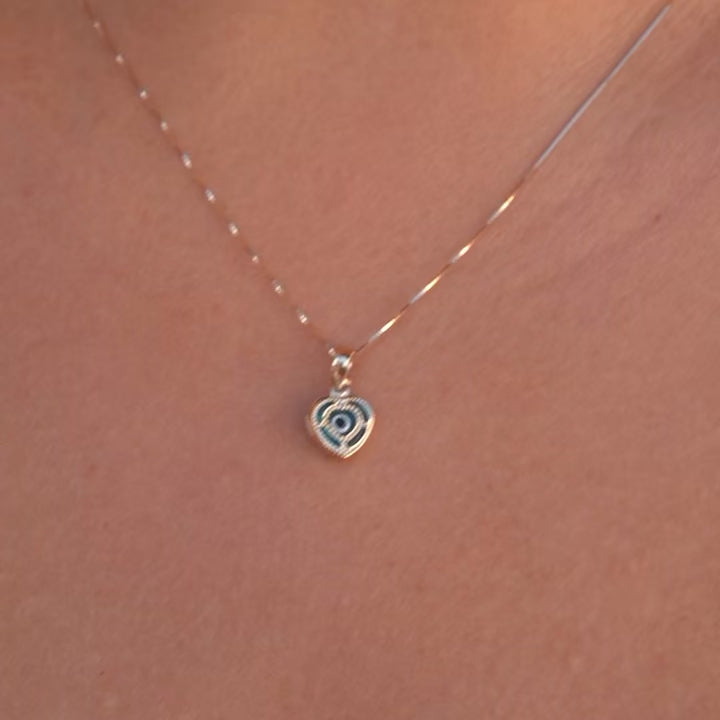 Model wearing a 14K yellow gold heart pendant with an evil eye center, showcasing elegant shine and dainty design against the skin.