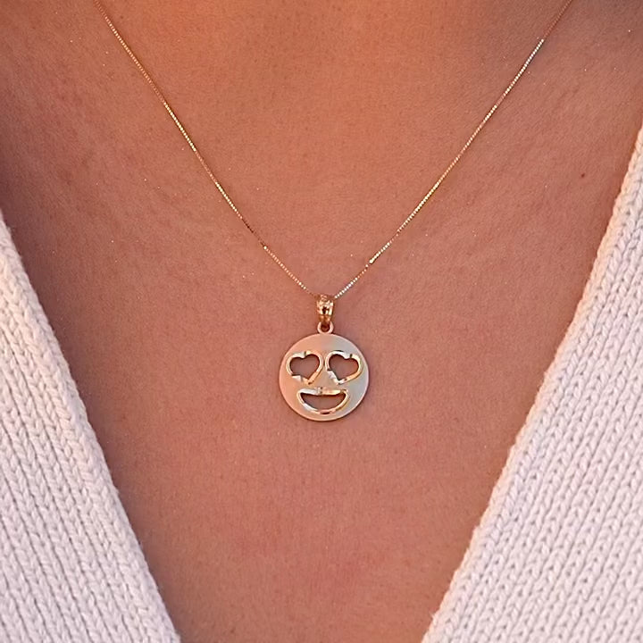 Video of a model wearing 14K gold heart eyes emoji pendant on a delicate gold chain, showing how the charm sits beautifully at the neckline for everyday elegance.