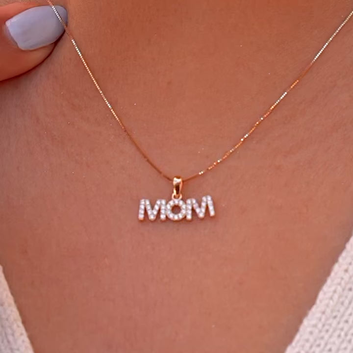 A model wearing a 14K Gold ‘Mom’ Pendant, featuring a graceful script design with cubic zirconia accents, displayed on a delicate chain. The pendant rests elegantly on the model’s neck, highlighting its polished finish and sentimental style.
