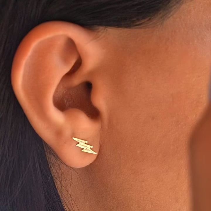 Model wearing 14K gold thunderbolt earrings, showcasing their trendy lightning bolt shape and dainty fit on the ear.
