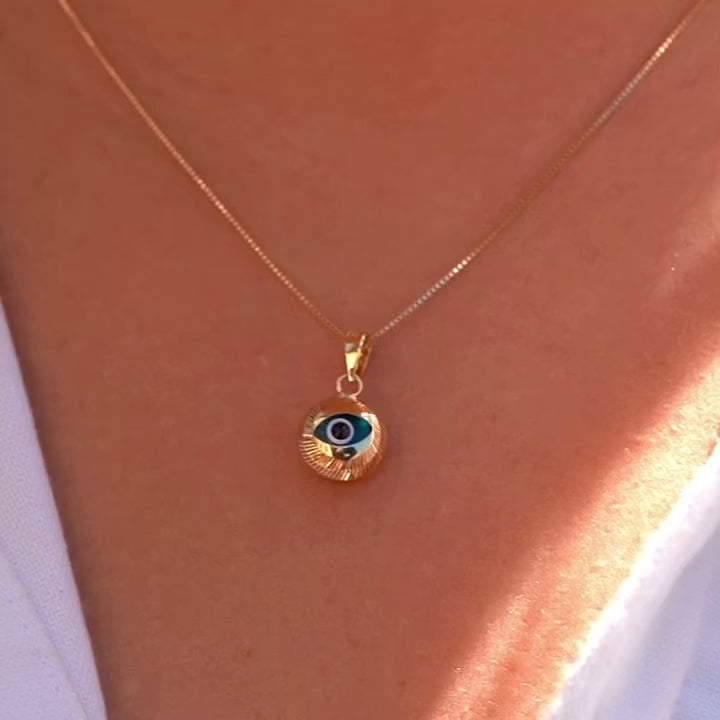 A model wears the 14K gold evil eye pendant with blue center on a fine chain, showcasing its dainty size and symbolic beauty as it rests just below the collarbone.