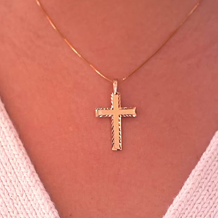 A model wearing the gold Latin cross pendant on a delicate chain, the charm sitting gracefully on her neckline with a soft glow.