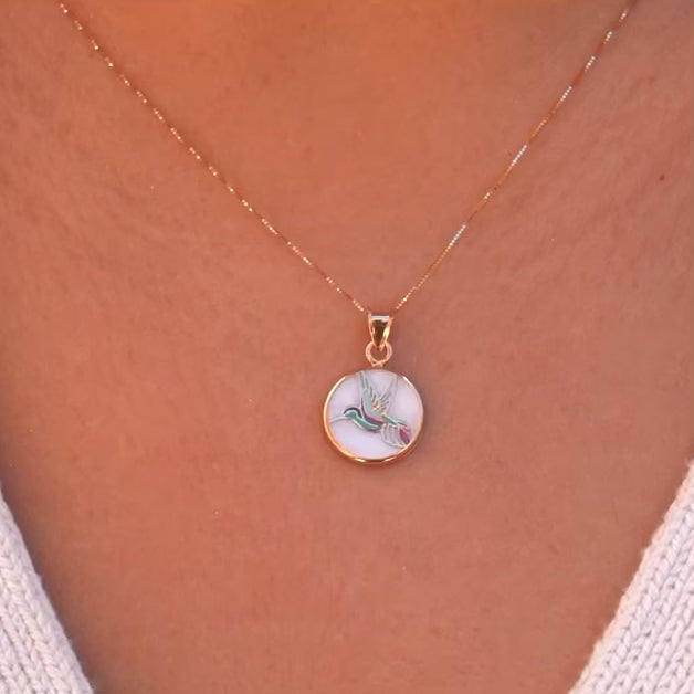 Model wearing the 14K Yellow Gold Hummingbird Medal Pendant on a delicate chain, showcasing the vibrant Mother of Pearl backdrop.