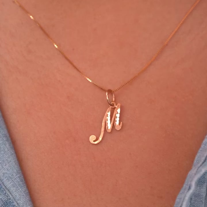 Model wearing a dainty gold initial M pendant, the charm sitting gracefully on her collarbone for a simple and personalized look.
