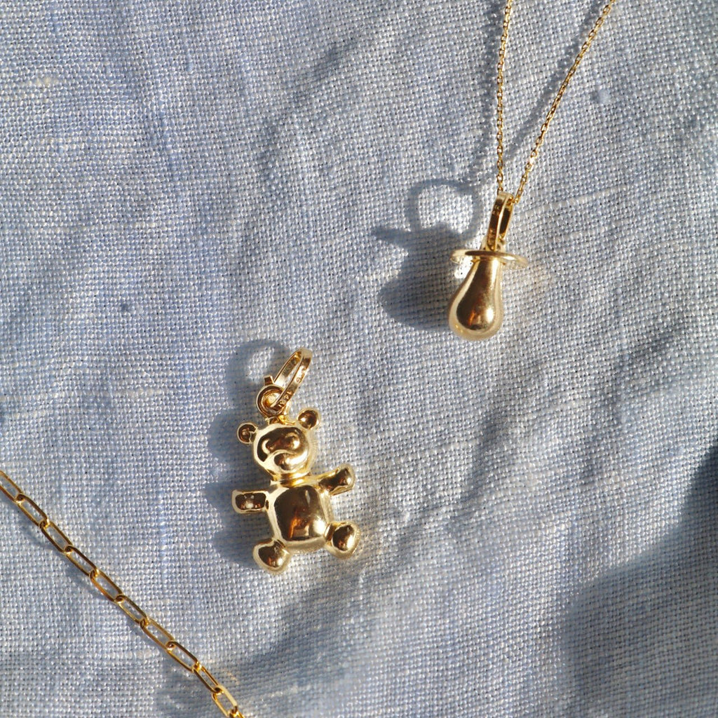 14K Real Gold Bear Pendant attached to a chain, elegantly laid on a textured textile surface to highlight its polished finish and delicate design.