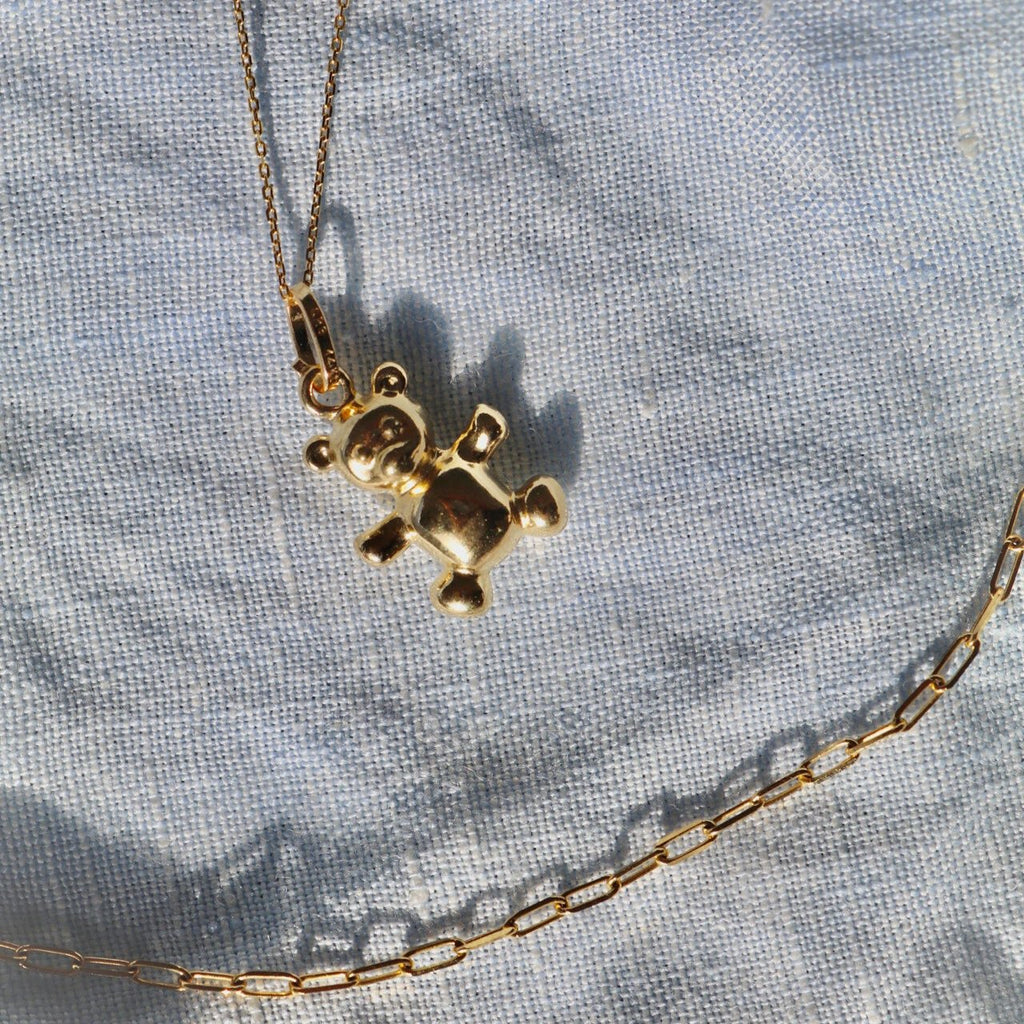 14K Real Gold Bear Pendant attached to a chain, elegantly laid on a textured textile surface to highlight its polished finish and delicate design.
