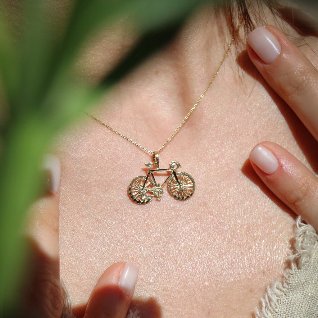 Model wearing the 14K Solid Gold Bicycle Charm on a chain, showcasing its intricate details and polished finish in a close-up view.