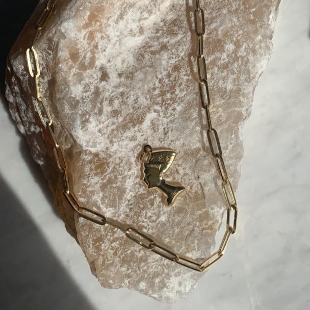14K Real Gold Nefertiti Charm displayed on a stone, highlighting its intricate details and polished gold finish against a natural backdrop.
