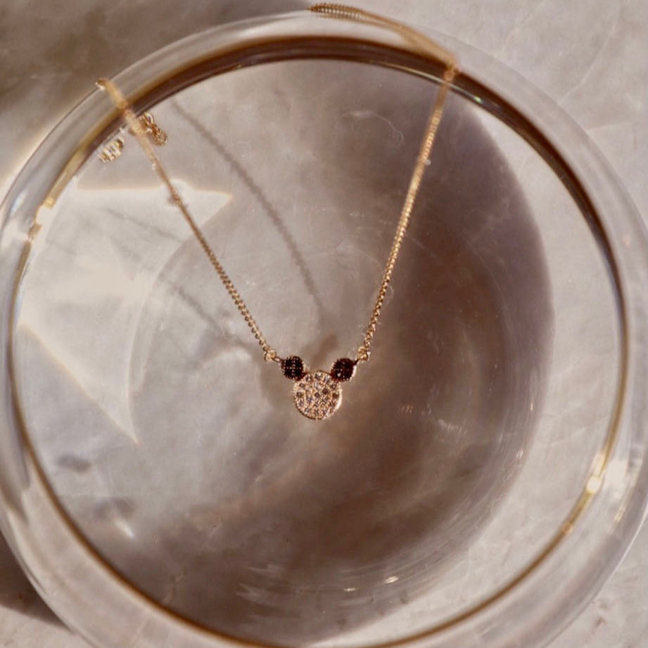 14K Solid Gold Mouse Necklace elegantly laid on top of a glass surface, showcasing its dainty mouse pendant and polished yellow gold chain.